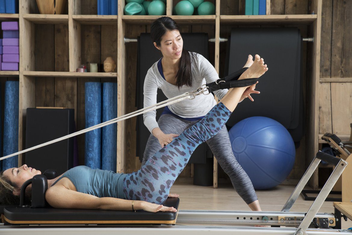 Pilates teacher assists student using reformer for leg exercises. Are Pilates Effective For Weight Loss